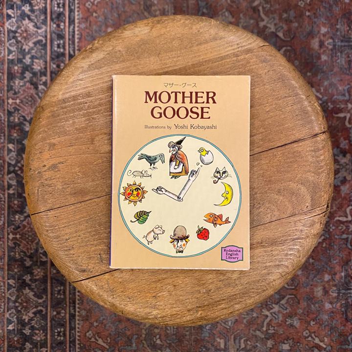 Bilingual Mother Goose paperback with a clock-face cover on a wooden stool