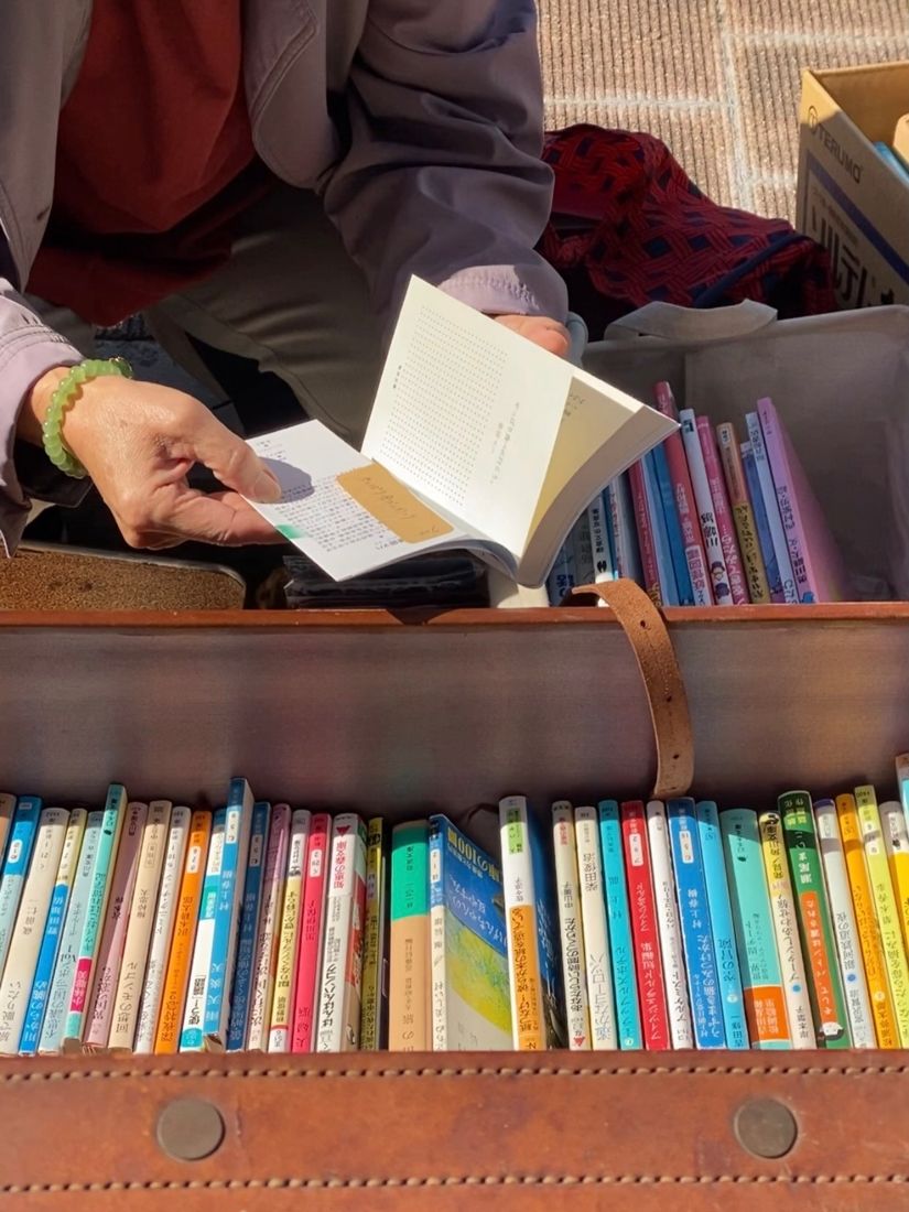 Hands leafing through a paperback above a vintage leather suitcase full of books